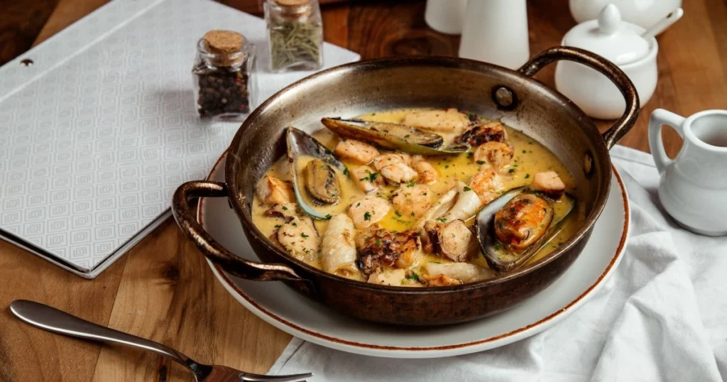 Detailed close-up photograph of a variety of fresh, high-quality mixed seafood, including shrimp, scallops, mussels, and white fish fillets. The seafood is arranged on a rustic wooden surface, with a warm, natural lighting illuminating the scene. The image focuses on showcasing the vibrant colors, textures, and visual appeal of the seafood, highlighting its nutritional benefits. The background is slightly blurred, drawing the viewer's attention to the center of the frame. The overall mood is one of culinary elegance and healthfulness. Seafood Mix Recipe